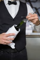 Bartender using corkscrew to open wine bottle in bar